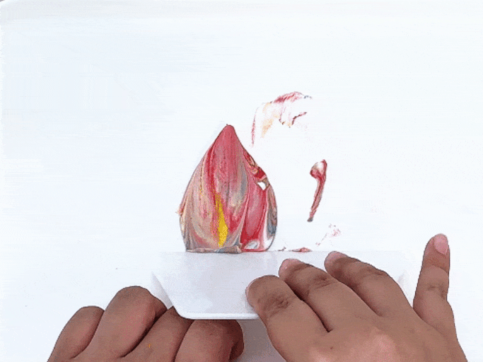 On a light woodgrain table, a white sheet of paper features several red and green apple prints, each adorned with googly eyes and simple, drawn-on arms and legs, giving them the appearance of dancing or moving apples. Above the paper lie two cut apple halves, one red and one green, the tools used to create the prints. This charming scene showcases a completed apple printing art project for children.