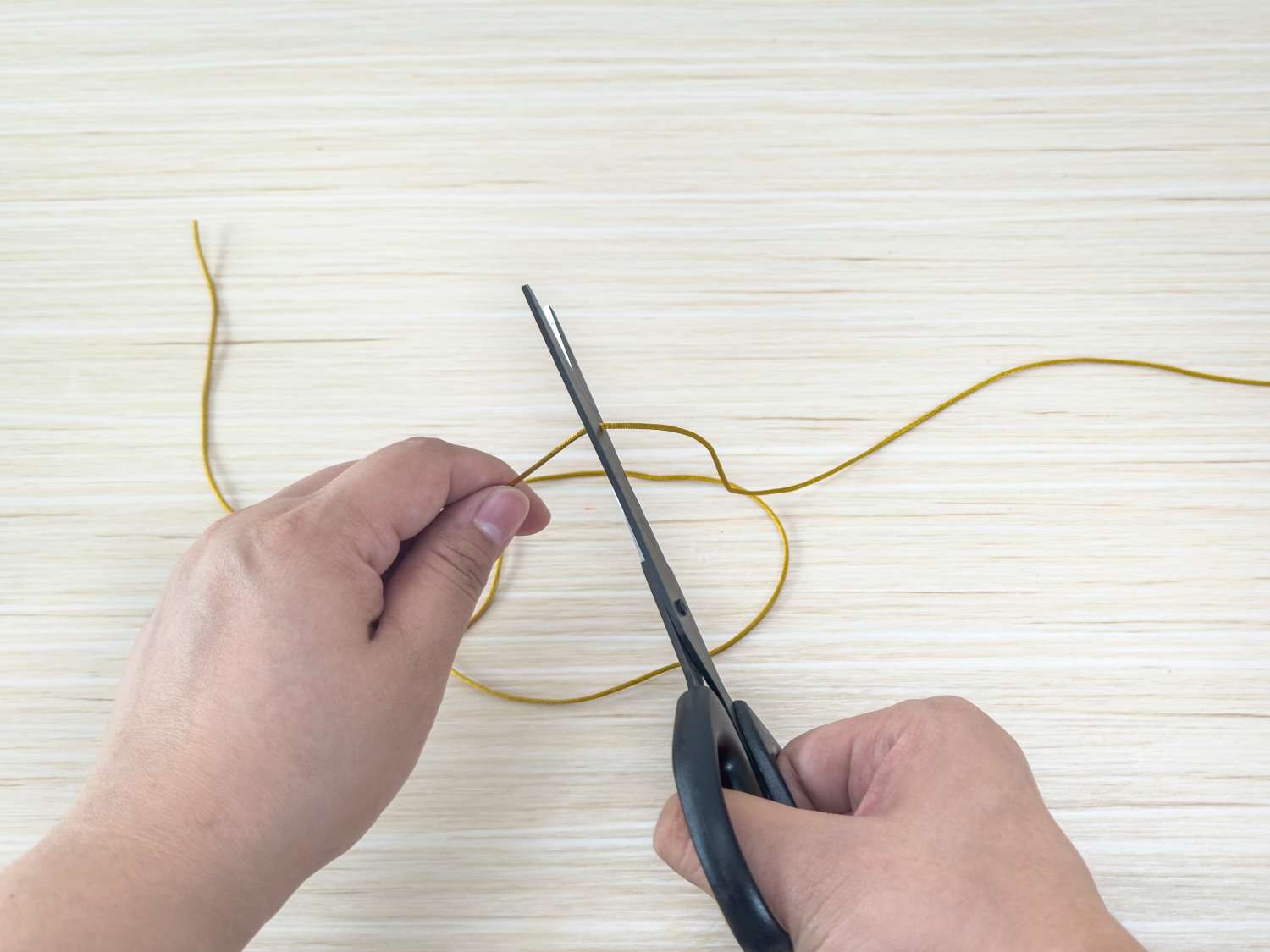 A person uses scissors to cut a length of gold cord.