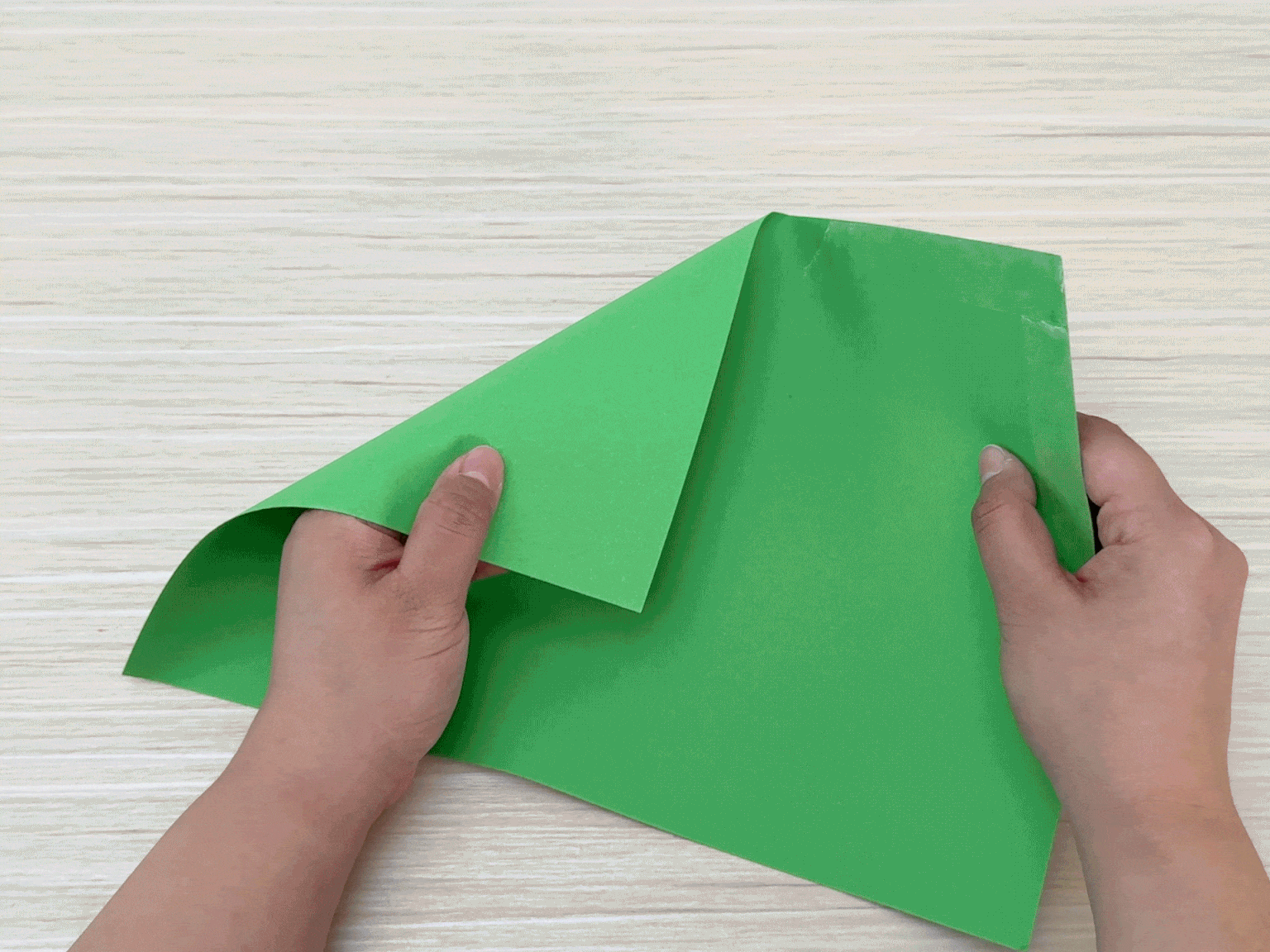 A person's hands are shown folding a sheet of bright green paper in half.