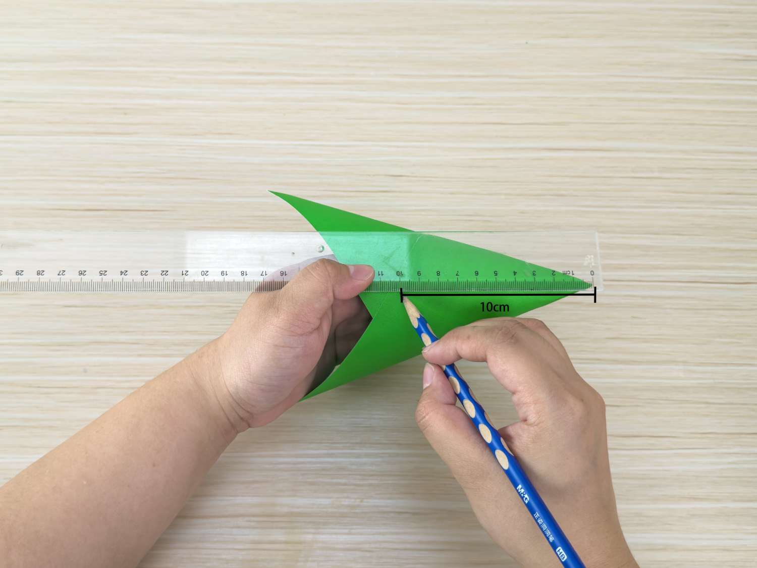 A person uses a ruler and pencil to mark a 10cm line on a folded piece of green paper.
