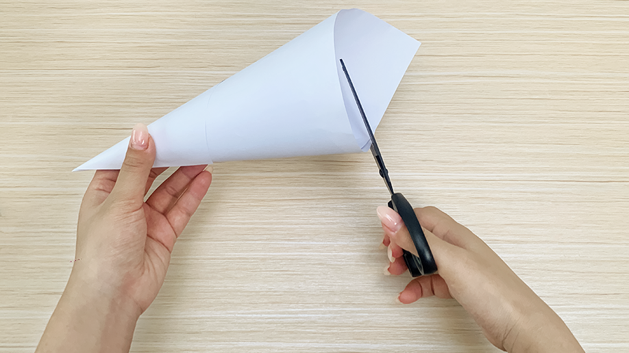 Snip, snip, hooray! A pair of hands carefully trims the excess paper from a cone shape, ensuring a neat and precise finish for the festive night light project. Nearly ready for the next step!