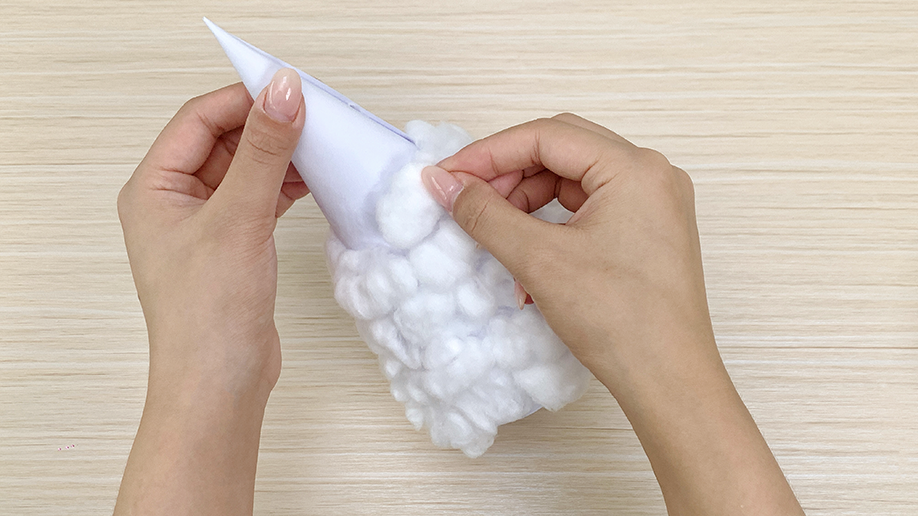 Adding the fluffy magic! Hands carefully and lovingly attach cotton balls to the paper cone, creating the charming, snowy texture of a miniature Christmas tree. It's starting to look festive!