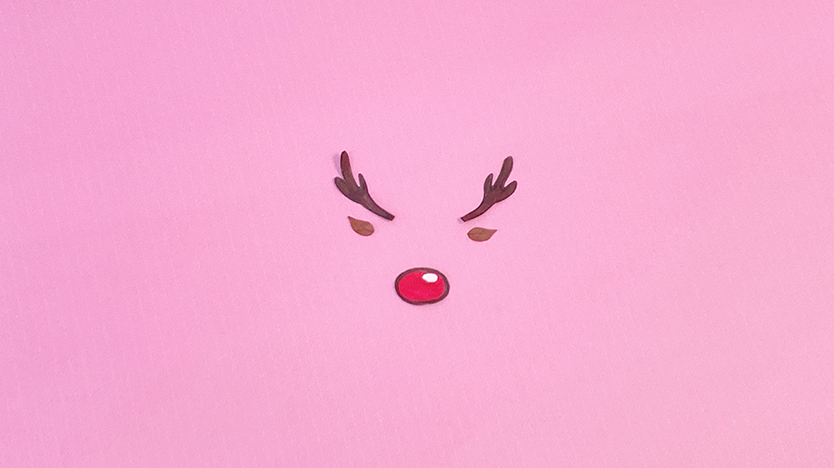 Adding the finishing touches! A cheerful reindeer face, complete with antlers and a bright red nose, has been carefully arranged on a pretty pink background. Looking rather dashing, wouldn't you say?