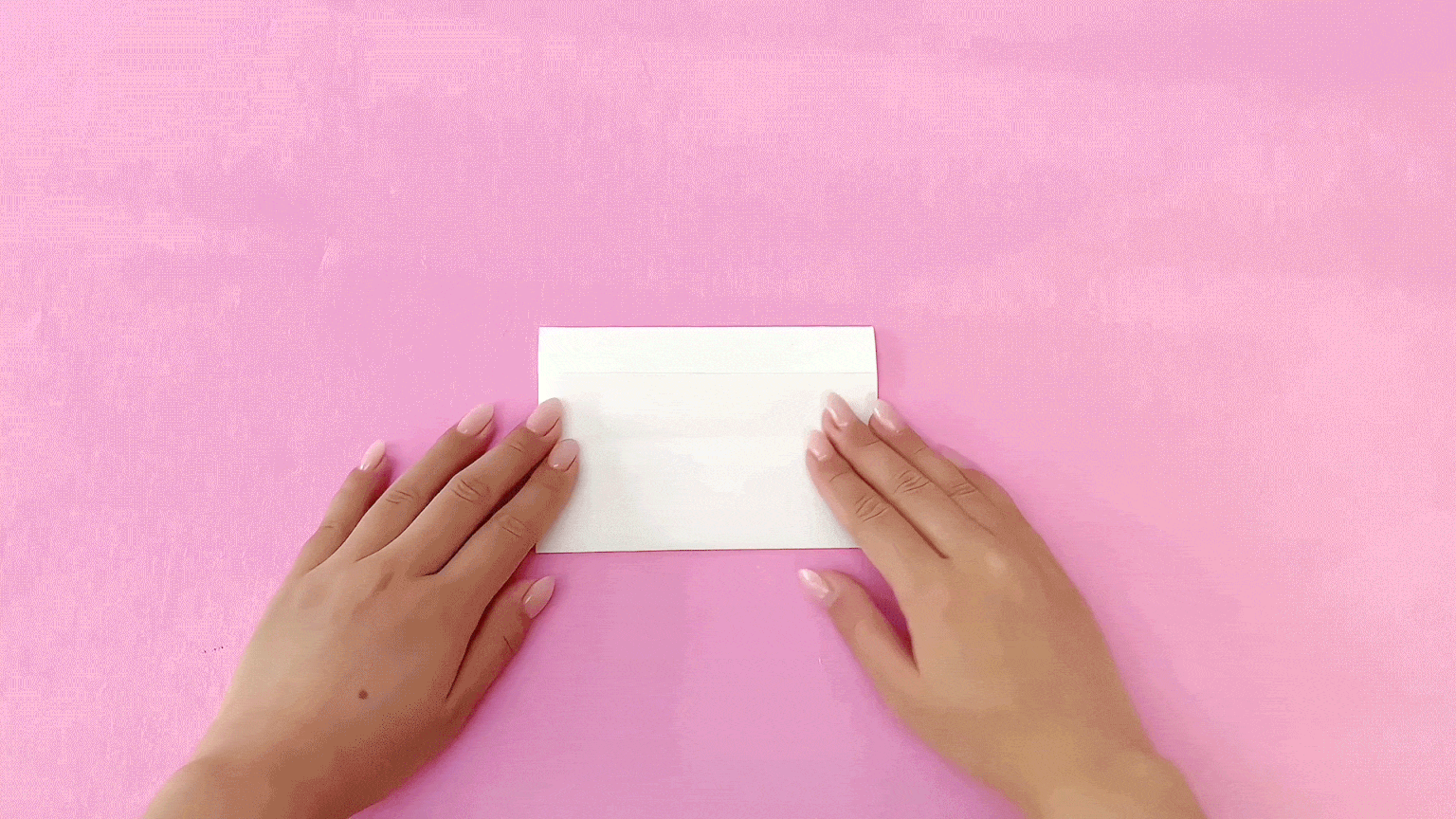 Making a neat fold! A pair of hands carefully creases the centre of a rectangular piece of white paper, ensuring a crisp and even fold for the next stage of the dancing reindeer construction. It's all coming together nicely!