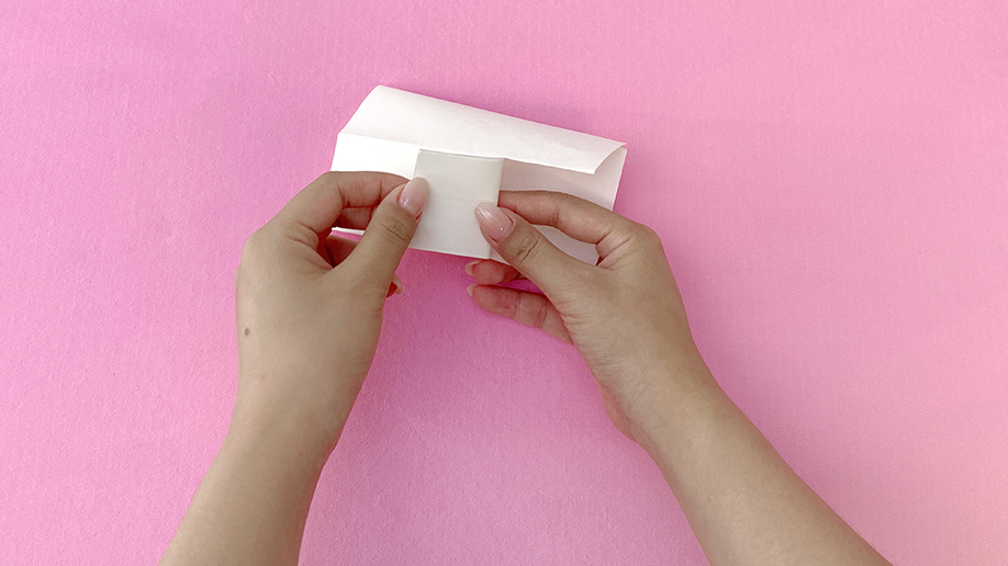 Adding the finishing touch! A pair of hands carefully secures a small square of paper to the folded base, creating a neat and secure pocket for the dancing reindeer's body. It's all coming together beautifully!