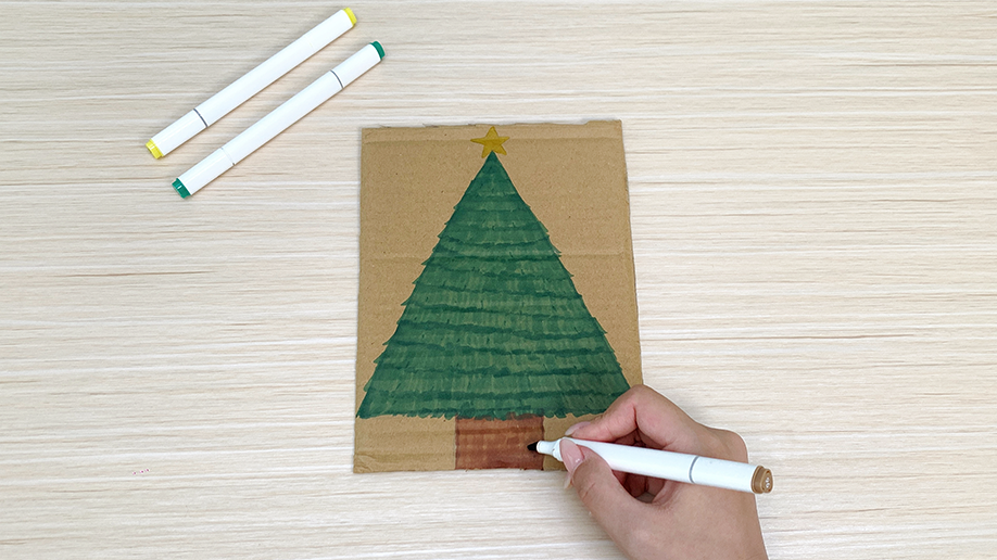 A hand uses a brown marker to carefully add the finishing touches to the tree trunk, completing this festive design on a piece of card. It's all shaping up rather nicely, wouldn't you say ?