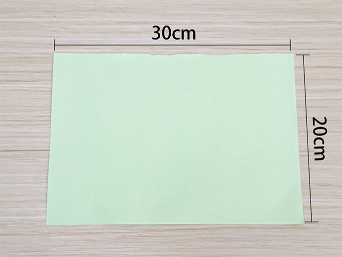 A light green rectangular piece of paper, measuring 30cm by 20cm, rests on a light wood grain surface. Lines and labels indicate the paper's dimensions. This image shows a sheet of paper ready for a craft or other project.