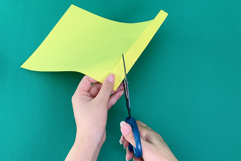 In this image, a person is cutting a piece of yellow paper with scissors, carefully shaping it for a craft project. The paper appears to be folded, allowing for the creation of symmetrical shapes or designs once cut. This simple step is often part of a larger craft, such as making paper decorations or figures. With just basic materials like coloured paper and scissors, this activity is easy and enjoyable for all ages, encouraging creativity while being perfect for school projects, home décor, or seasonal crafts.