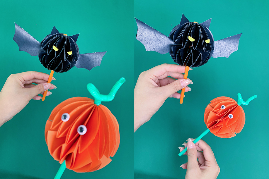 In this image, two playful Halloween crafts are shown: a paper bat and a paper pumpkin. The bat is crafted from black paper, with its body formed into a 3D spherical shape, complete with wings, pointed ears, and yellow eyes. It is attached to an orange straw for easy handling. The pumpkin, made from orange paper, is also shaped into a 3D sphere and decorated with googly eyes and a green pipe cleaner for the stem. These simple and fun Halloween crafts are perfect for children and adults, requiring only a few materials such as coloured paper, glue, and pipe cleaners. They make for charming Halloween decorations or props for festive games and activities.