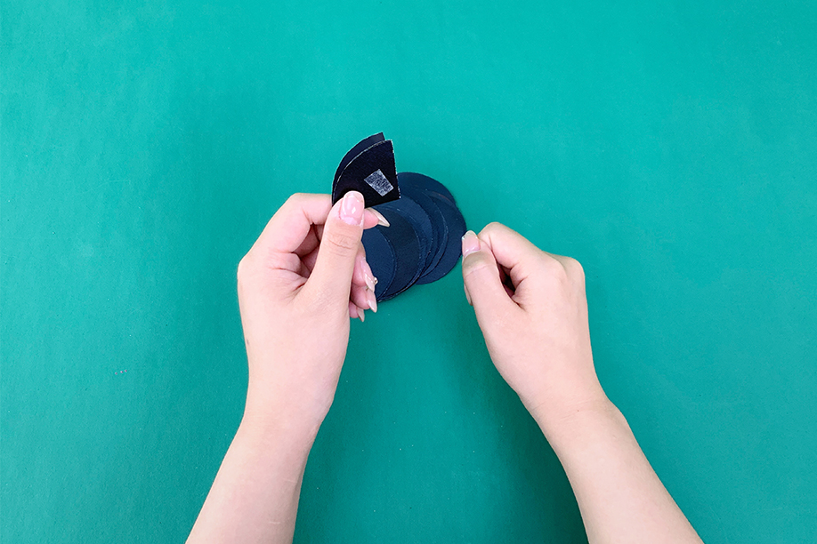 In this craft activity, a person is assembling the body of a paper bat using circular pieces of black paper. The hands are carefully folding and attaching the bat's parts, with a small adhesive strip visible to secure the pieces together. This simple and fun craft is perfect for Halloween decorations, allowing crafters of all ages to create their own spooky bats with just a few basic materials such as paper, glue, and tape. The end result can be used to add a playful and festive touch to any space, making it a delightful homemade decoration for the Halloween season.