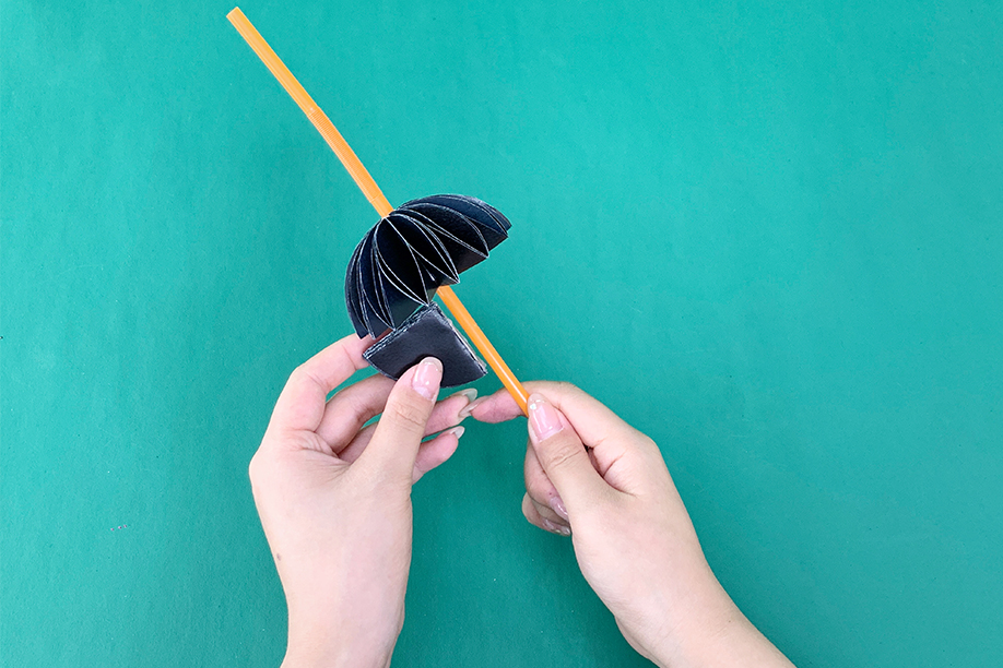 In this image, a person is putting the finishing touches on a paper bat craft by attaching the body to a pencil. The bat’s wings are made from folded black paper, creating a 3D effect, while the body is being secured with an adhesive strip. This simple yet creative craft is perfect for Halloween, offering a fun and easy way to make spooky decorations with minimal materials. Ideal for children and adults alike, this DIY project adds a playful and festive element to pencils, making them perfect for Halloween-themed activities or as a decorative touch to stationery.