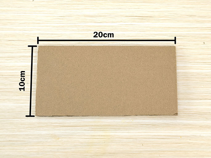A rectangular piece of light brown cardboard lies on a light wood surface. Black lines indicate the dimensions of the cardboard: 20cm wide and 10cm tall. The image is a simple depiction of a piece of cardboard with its measurements clearly marked.