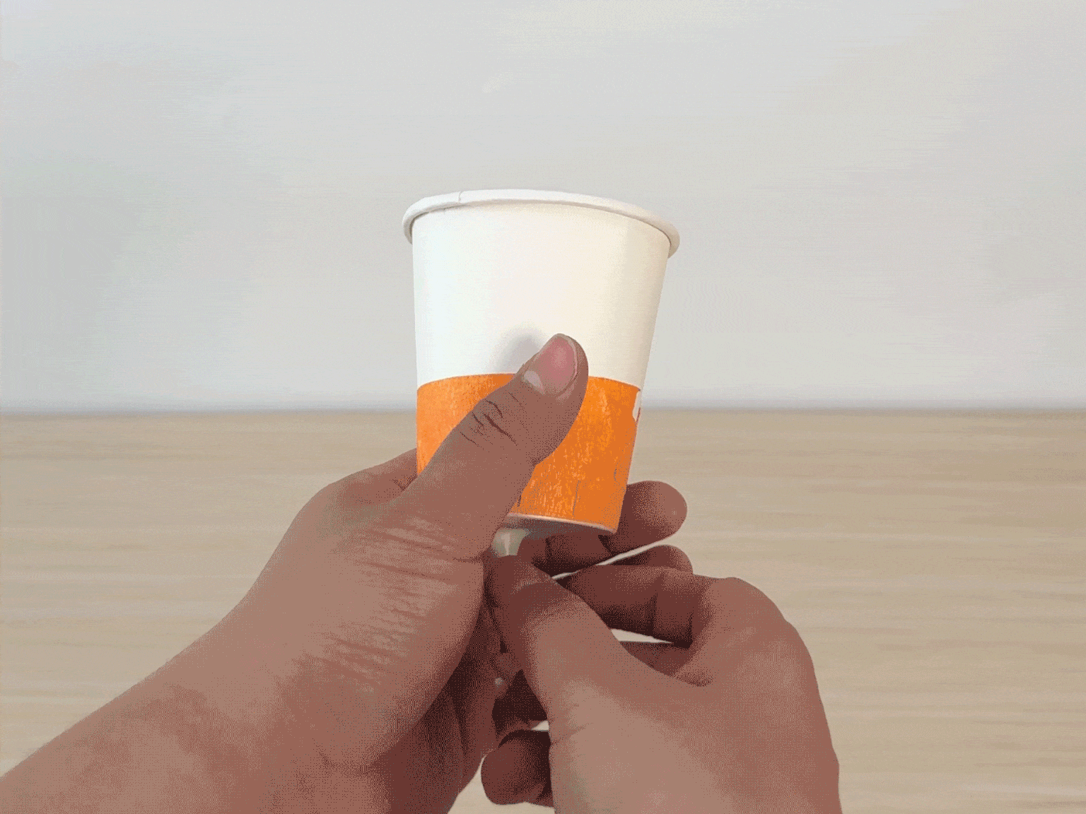 A hand holds a white paper cup with an orange band around its middle. The cup is attached to a balloon, and as the balloon is inflated and released, colorful confetti shoots out from the cup, creating a festive burst.