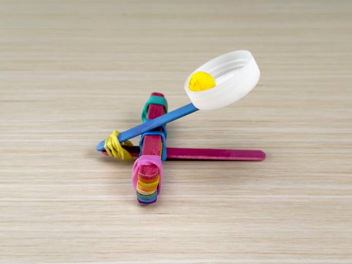 Two hands hold a completed red origami mouse, its body made of folded segments and a small, pointed tail. A small, pink origami object is visible in the top left corner.