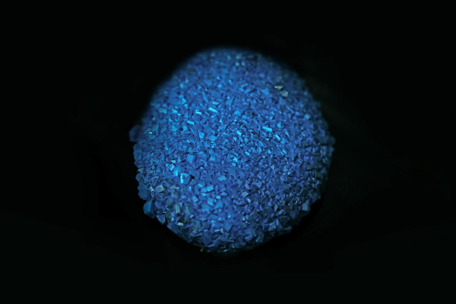 A close-up reveals a dark blue, crystal-like object, resembling a cluster of small,faceted gems, set against a black background.