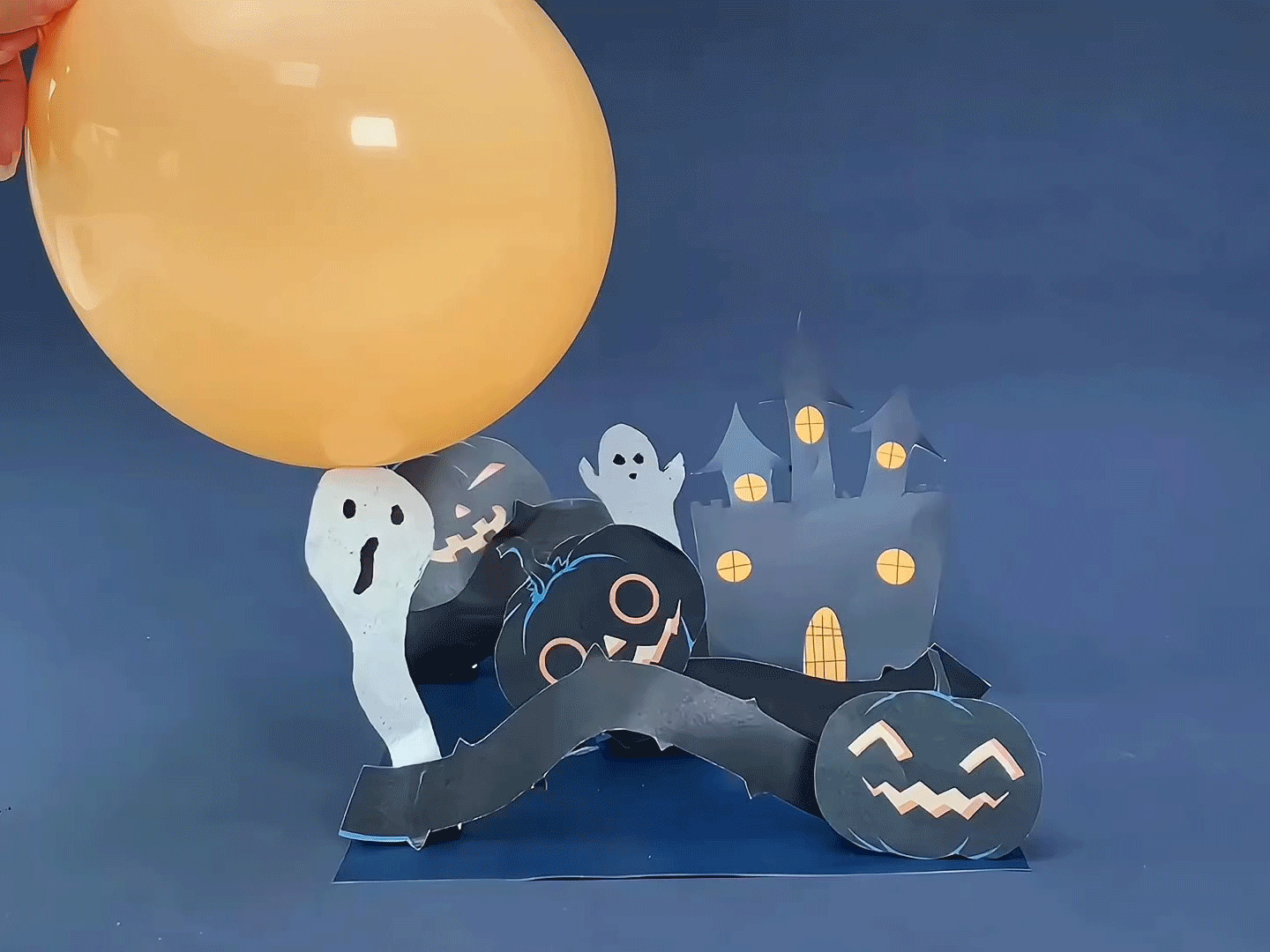 A Halloween diorama featuring a paper castle, ghosts, pumpkins, and bats is displayed, with an inflated orange balloon positioned above it, possibly representing the moon.