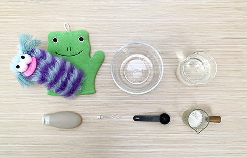 Gather your bubbly bits and bobs! We'll need a frog puppet (for extra charm, of course!), a fluffy monster toy, a bowl, a jug, a small bottle of liquid, a pipette, a measuring spoon, and a container of cornflour. Let's get those bouncing bubbles brewing!