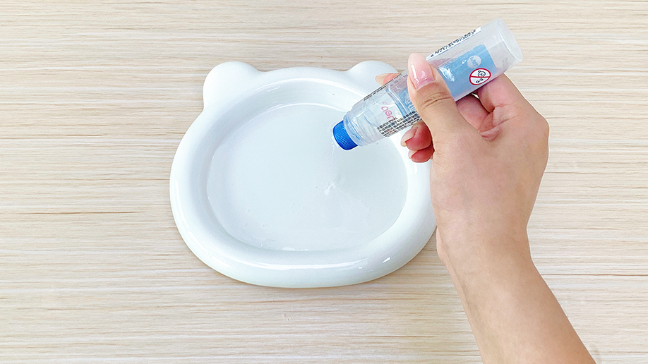 Adding the magic ingredient! A hand carefully pours clear glue into a small, bear-shaped dish, preparing the surface for a spectacular miniature fireworks display. It's all systems go for some fizzy fun!