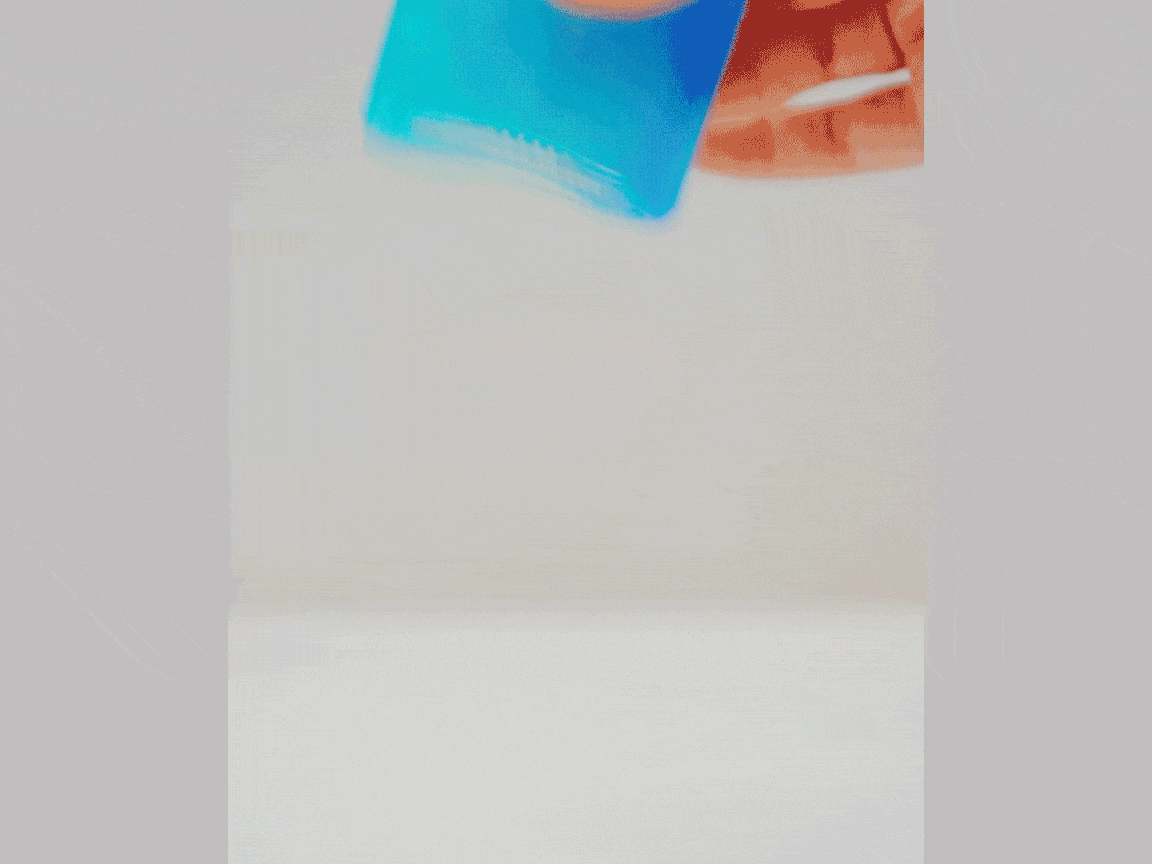 A small, clear glass bottle with a silver cap is filled with a vibrant blue liquid. When the bottle is placed upright, the liquid separates, gradually forming distinct layers of color, transitioning from a deeper blue at the bottom to a bright turquoise, then a lighter green, and finally a yellowish hue at the top. This visual demonstration likely showcases a density experiment or the layering of different liquids.
