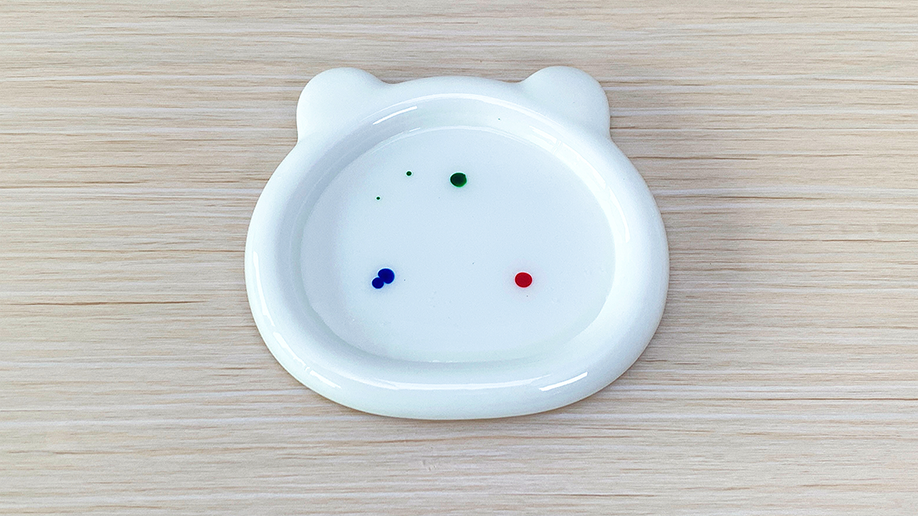 Splish, splash, splosh! Tiny droplets of red, blue, and green food colouring sit patiently in a shallow, bear-shaped dish filled with glue, ready to burst into a miniature fireworks display. Let's see what happens!