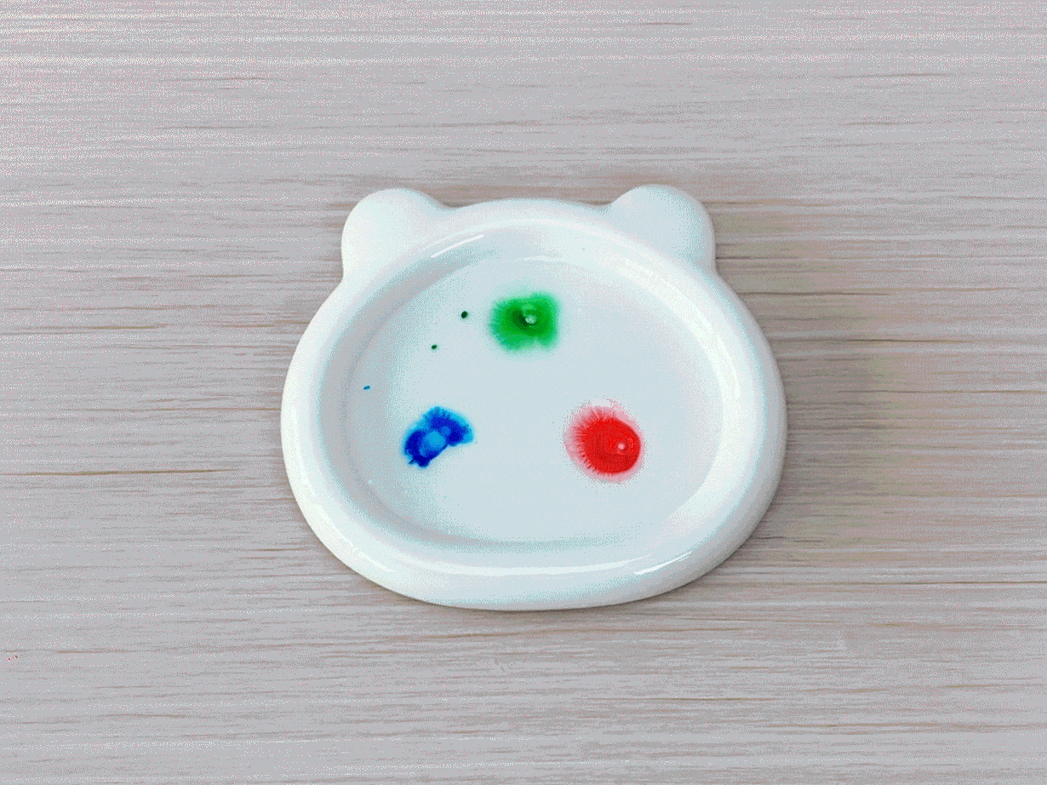 Ooh, look at that colourful concoction! Drops of vibrant red, blue, and green food colouring sit in a small, bear-shaped dish, ready to create a miniature fireworks display. Let's get those colours mixing!