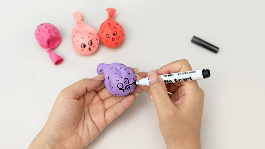 Adding some character! A hand uses a black marker pen to draw a cute face onto a purple balloon pufferfish, bringing a bit of personality to this spiky science project. Those are some rather charming expressions!