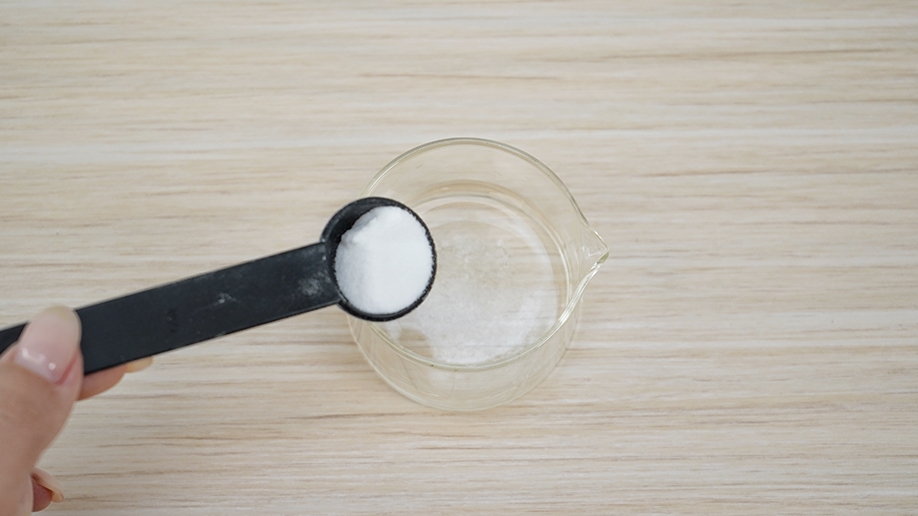 A hand carefully adds a spoonful of bicarbonate of soda to a small glass of water, creating the magic ingredient for our invisible ink. It's all rather hush-hush, innit?