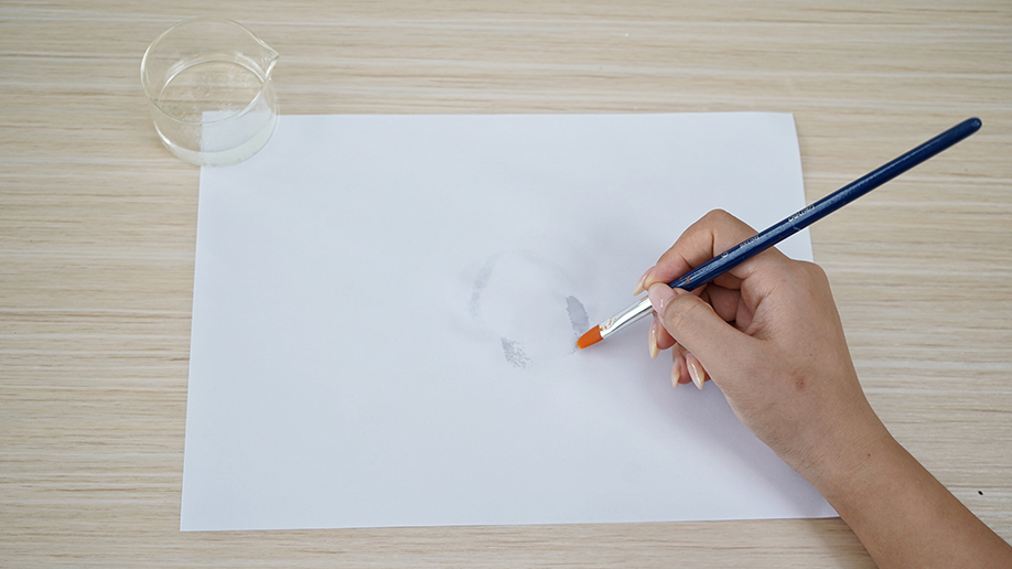 A hand carefully uses a paintbrush to apply the invisible ink to a sheet of paper, creating a hidden message that will only be revealed with a bit of heat. It's all rather hush-hush, innit?