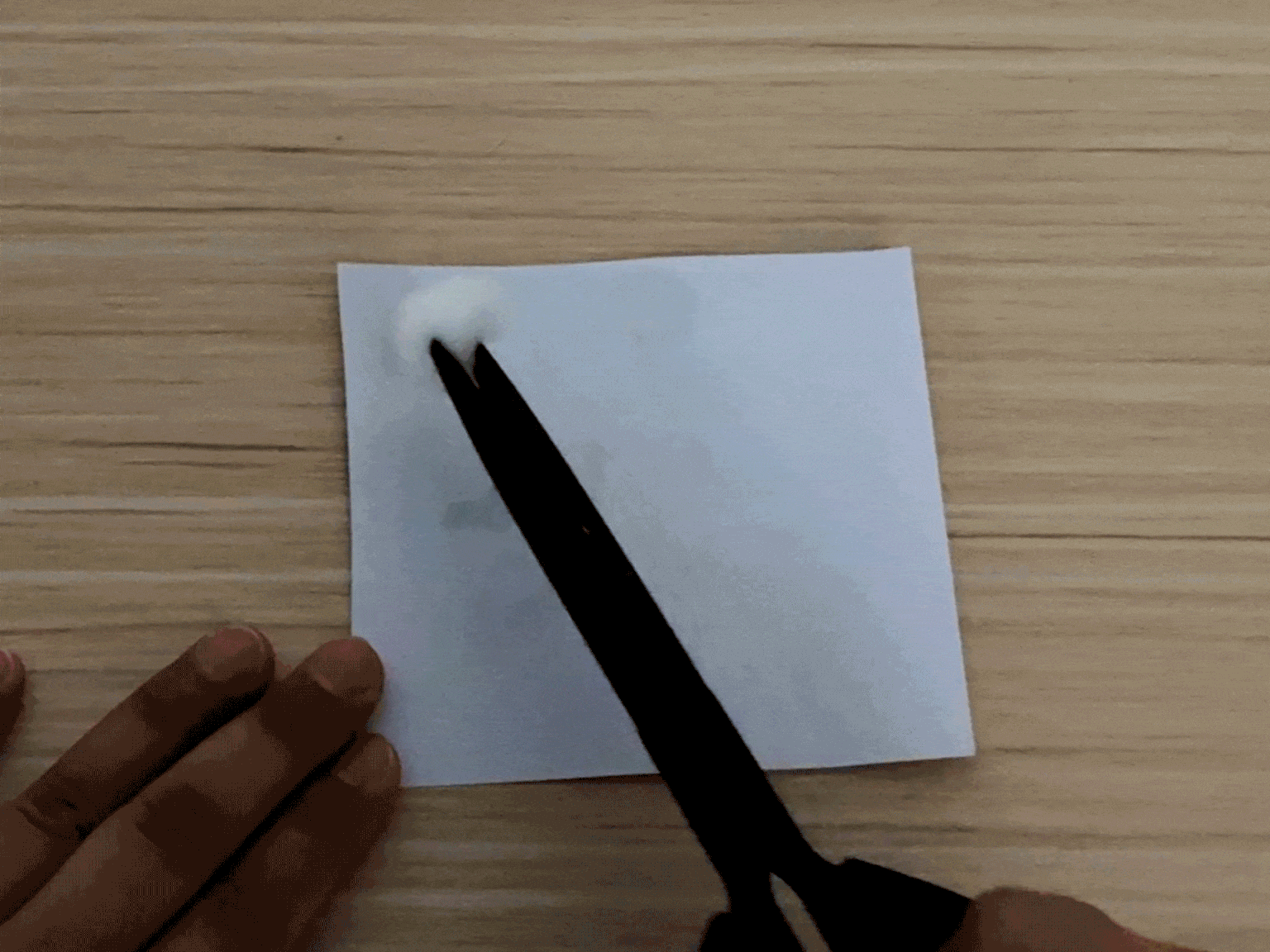 A hand uses a black marker or pen with a cotton ball attached to its tip to draw on a white piece of paper. The marker/pen leaves a bright, neon yellow or greenish-yellow trail. The hand draws simple shapes and lines, seemingly creating a drawing of a gift or present with a ribbon. The video shows a simple drawing activity using an unusual drawing tool.