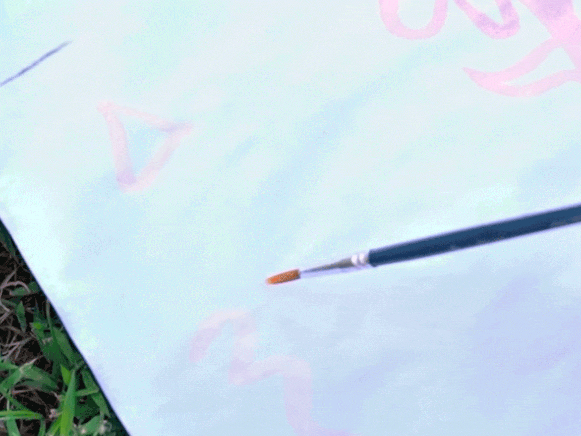 Ooh, look at that, a bit of artistic magic! A paintbrush is delicately adding some pale pink swirls and shapes to a piece of paper. It's all rather pretty, innit? A proper bit of creative fun!