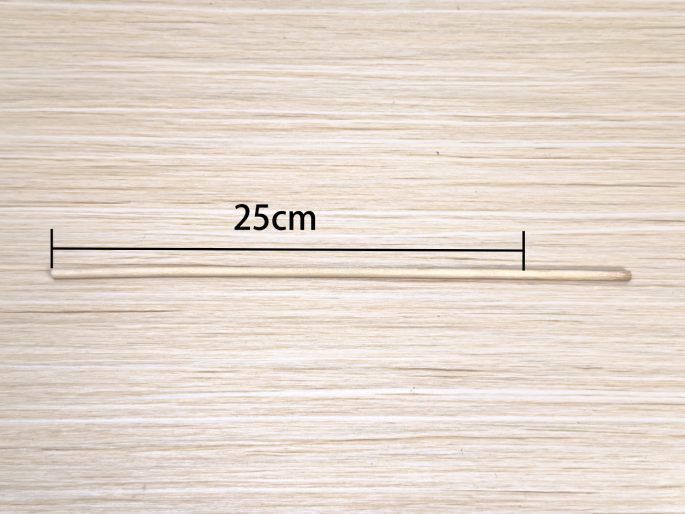 A thin, light-colored wooden dowel lies horizontally on a light wood-grain surface. A line above the dowel indicates its length, marked as 25cm. This image simply displays the dowel and its measurement.