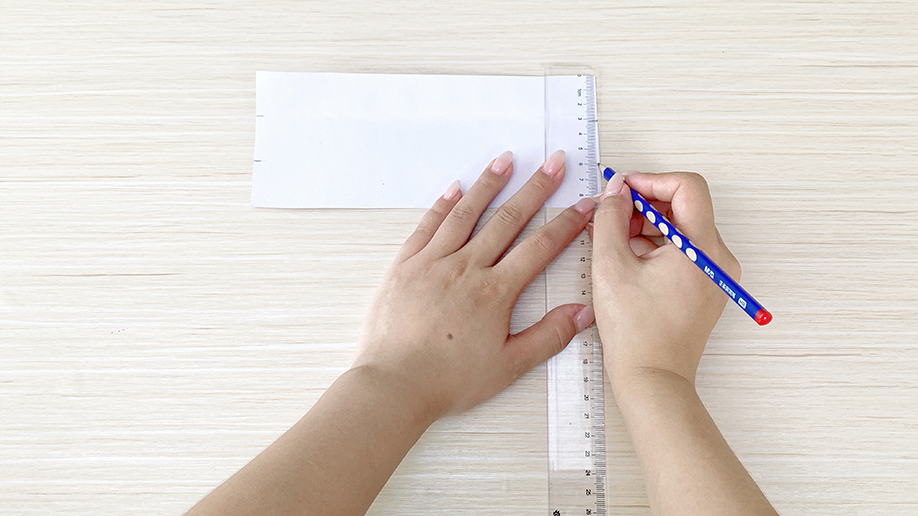 A steady hand uses a ruler and pencil to carefully mark a straight line onto a piece of paper; looks like the start of a precise craft project to me.