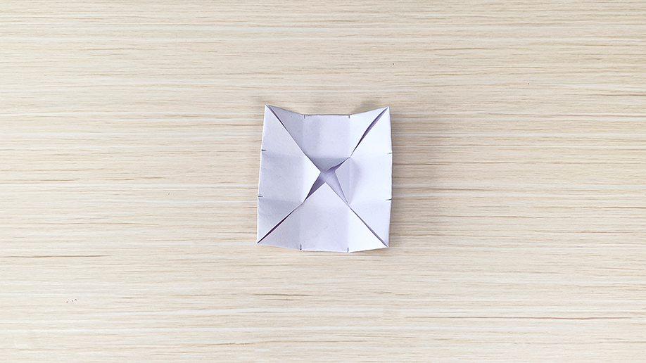 There's a bit of paper there, folded into a neat little square shape, all pointy and precise. It's sitting on a light wood surface, looking rather pleased with itself.