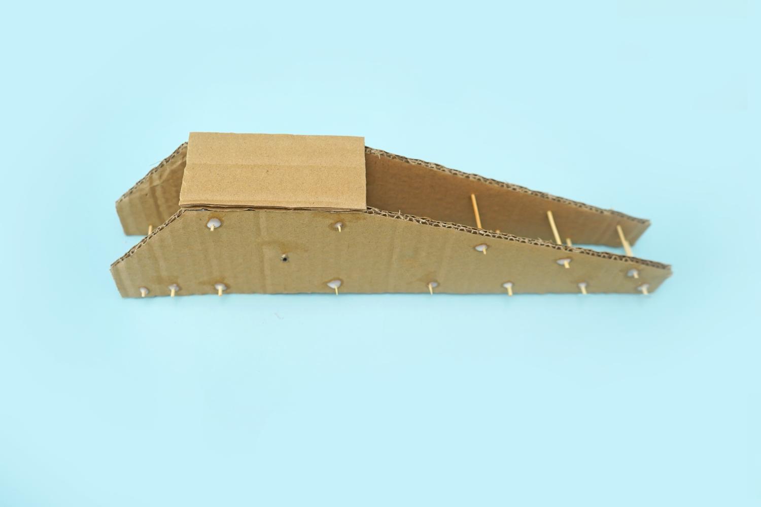 A cardboard structure, resembling a crane arm, with toothpicks glued into place, sits on a pale blue surface.