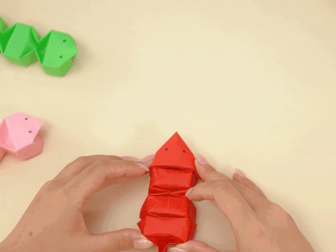 Ooh, look at that, a bit of paper folding magic! Someone's crafting a little red snake, and it's all rather clever, innit? Those little folds are making a right spiffing body. A proper bit of crafty fun!