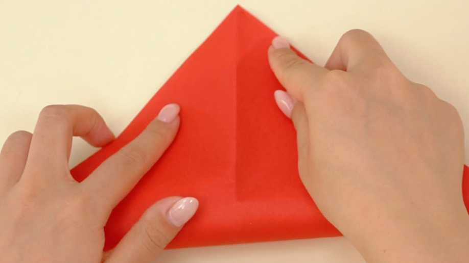 A bit of paper folding magic! Someone's carefully folding a piece of red paper into a neat little triangle. It's all rather precise, innit? A proper bit of crafty concentration!