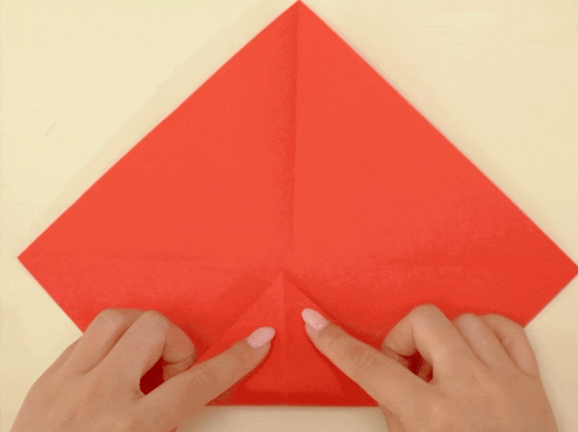Someone's carefully folding the red paper in half, making a neat little crease. It's all rather precise, innit? A proper bit of crafty concentration! I wonder what they're making?