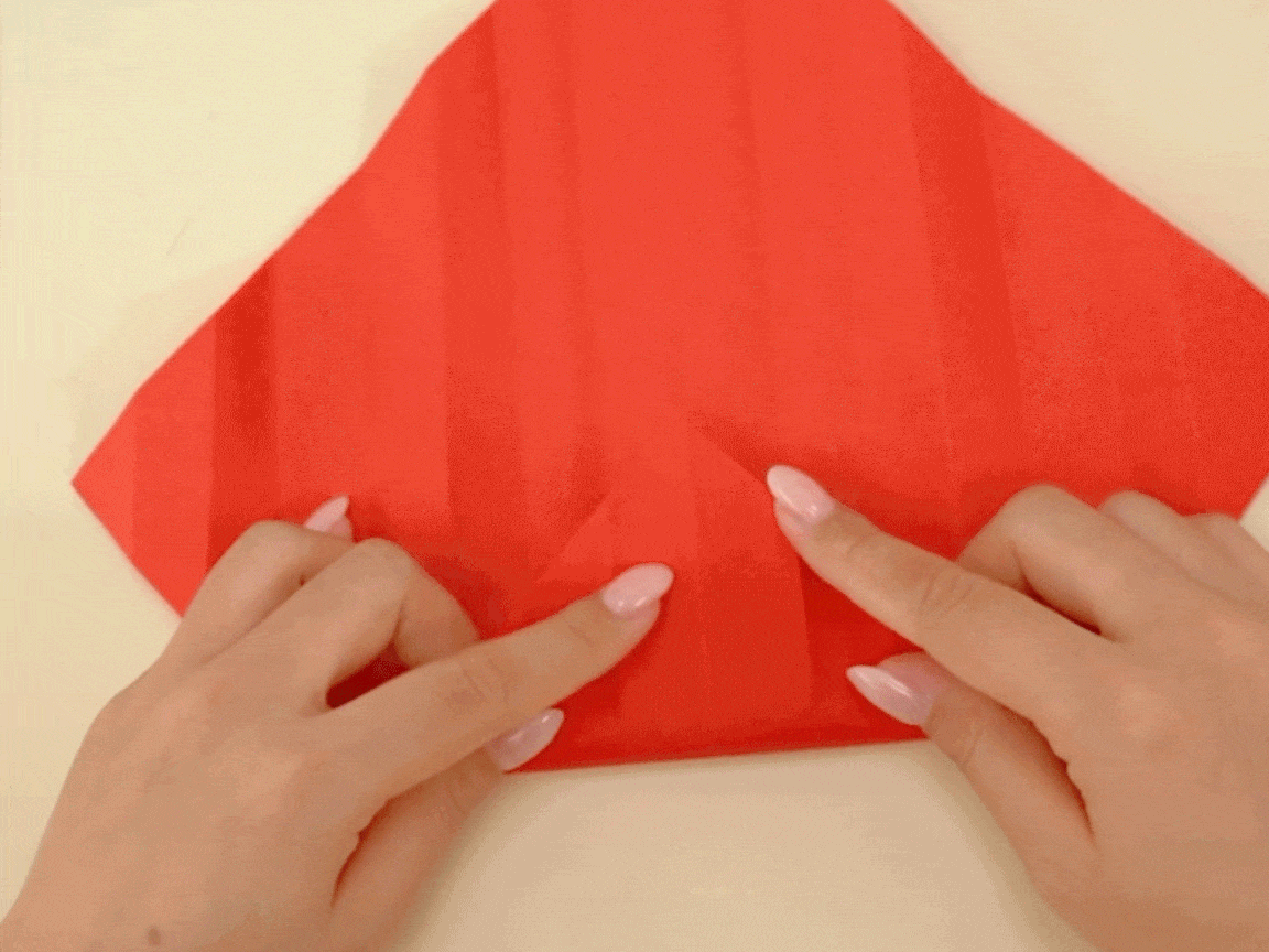 look at that, they're making a right neat little point! The red paper is being folded and creased with such precision. It's all rather satisfying to watch, innit? A proper bit of origami wizardry!
