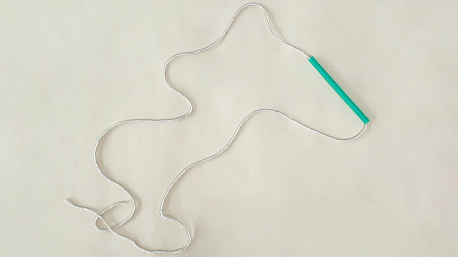 A length of white string or twine is loosely arranged on a cream background, with a short section of green straw threaded onto it.