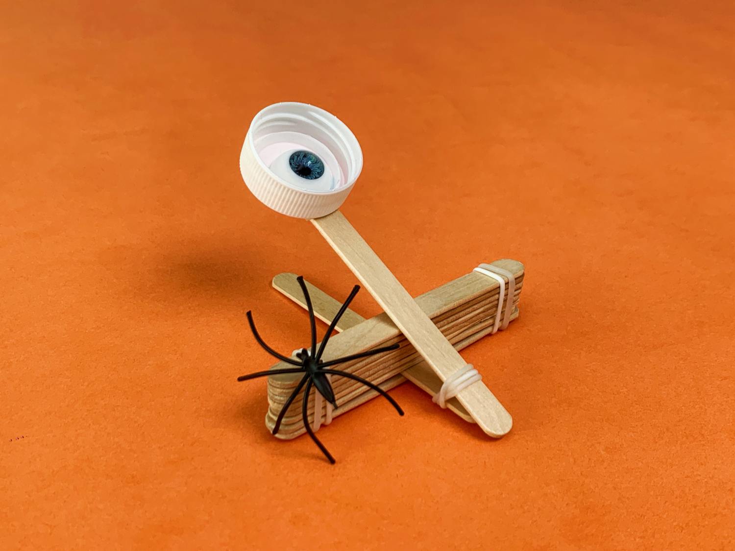 A spooky spider catapult, crafted from simple materials, is ready for action; a plastic spider waits to be launched from its ingenious, craft-stick base.