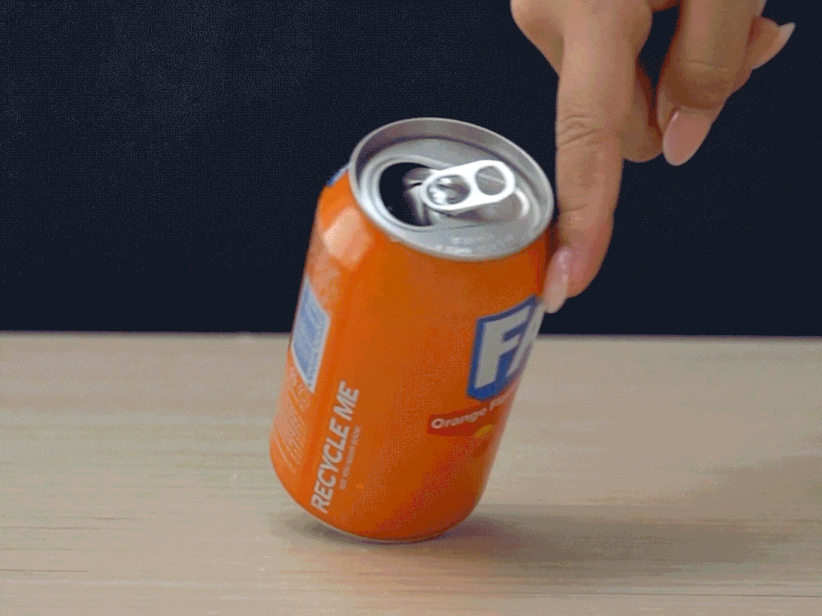 A hand spins an open, partially full can of Fanta on a table.
