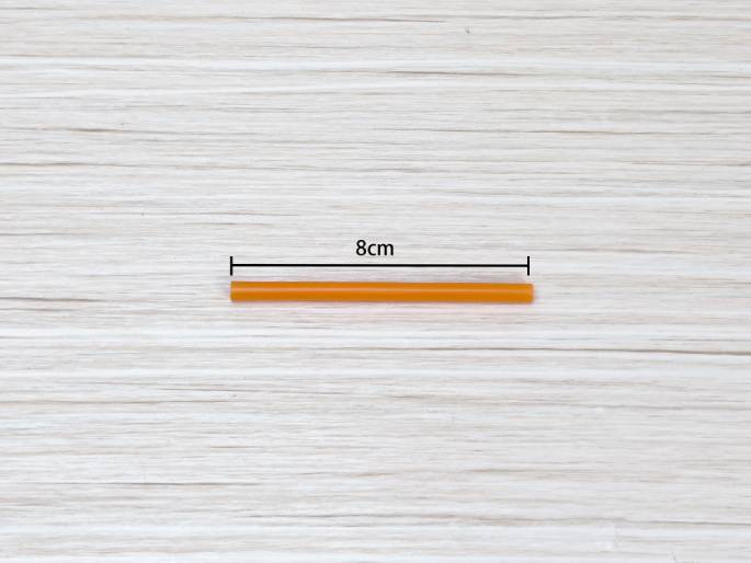 An 8cm long orange stick or dowel lies horizontally on a light wood grain background. Lines and the label 8cm indicate its measurement.