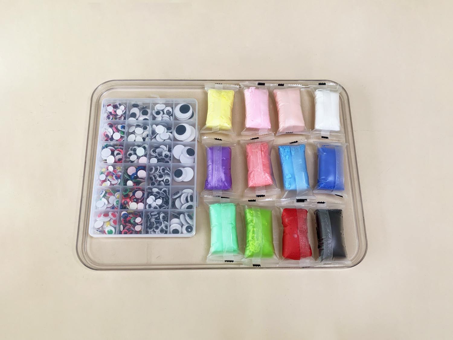 A clear plastic tray holds a container of assorted googly eyes and small packets of colourful playdough or modelling clay.