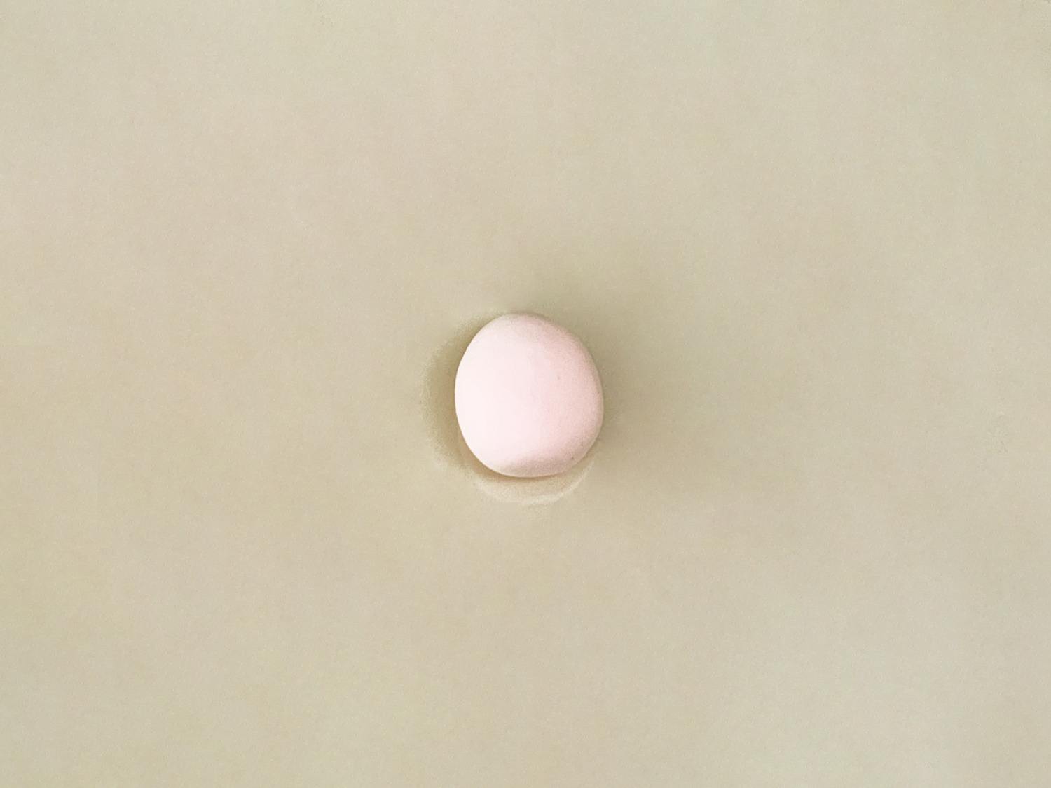 A small, pale pink ball of playdough rests on a plain, light beige surface.