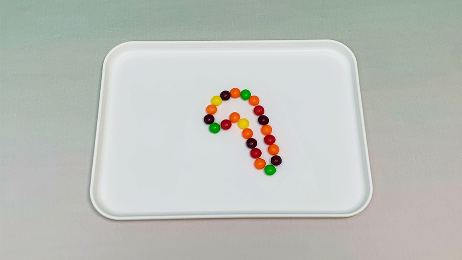 Multicoloured Skittles are arranged in a question mark shape on a white tray.