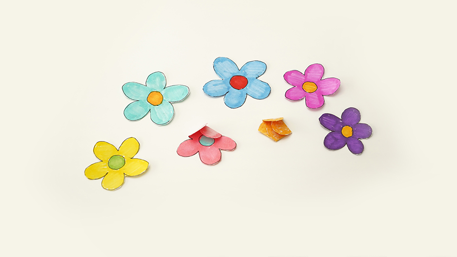 Several colourful paper flowers, some folded and some unfolded, are scattered on a white surface.