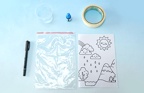 A clear plastic bag, a small cup, a bottle of blue liquid, a roll of tape, a black marker pen, and a sheet of paper with a drawn water cycle scene are arranged on a pale blue surface.