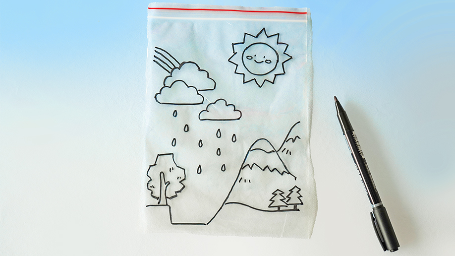 A clear plastic bag, with a hand-drawn picture of a simple water cycle scene on it, lies on a white surface next to a black marker pen against a pale blue background.