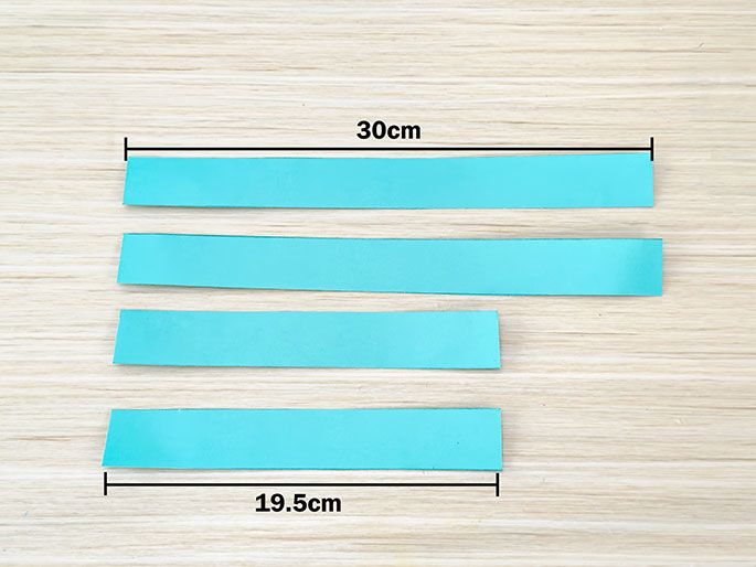 Four teal-colored paper strips are arranged horizontally on a light wood-grained surface. The strips are evenly spaced. A line indicating their length (30cm) is drawn above the top strip, and another line indicating their width (19.5cm) is drawn below the bottom strip.