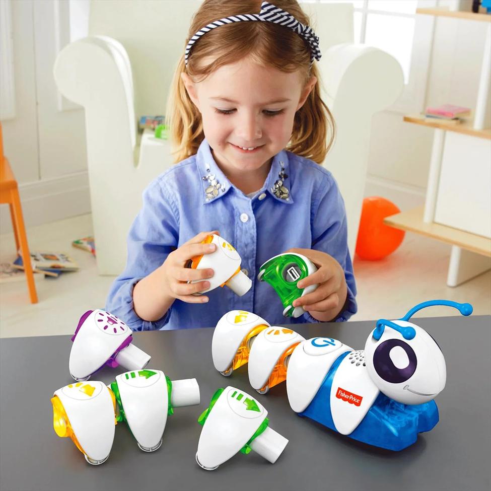 A young girl assembles a colourful, segmented toy caterpillar, likely a coding or programming toy, on a table.